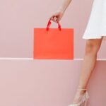 Clearance Sales - Crop anonymous stylish female in white dress and high heels carrying red shopping bag against pink wall